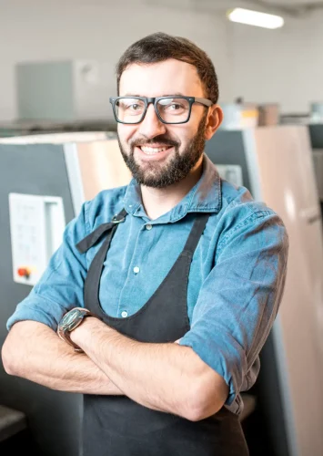 Portrait of a handsome typographer standing at the printing manufacturing with offset machine on the background