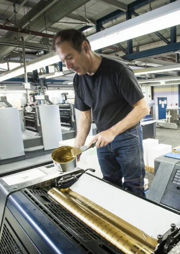 Worker applying gold ink to printing machine in print workshop